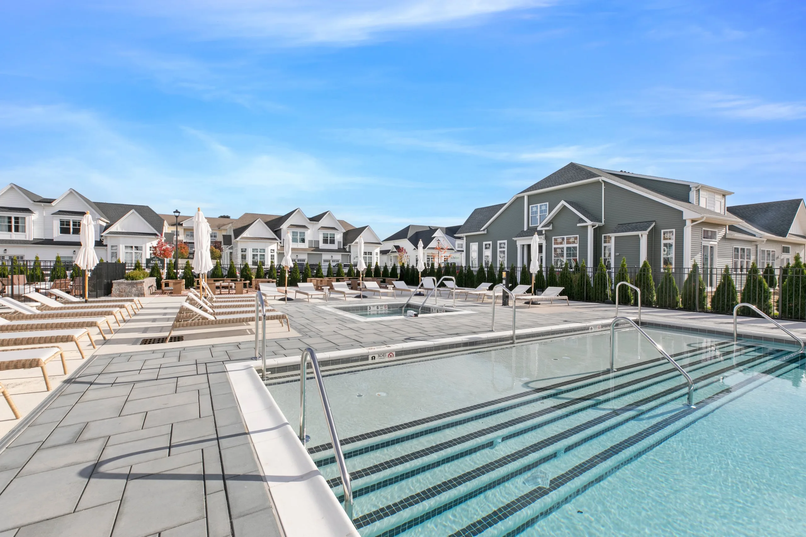 Wide entry steps into the clubhouse pool with stainless handrails, a spa and lounge chairs behind it