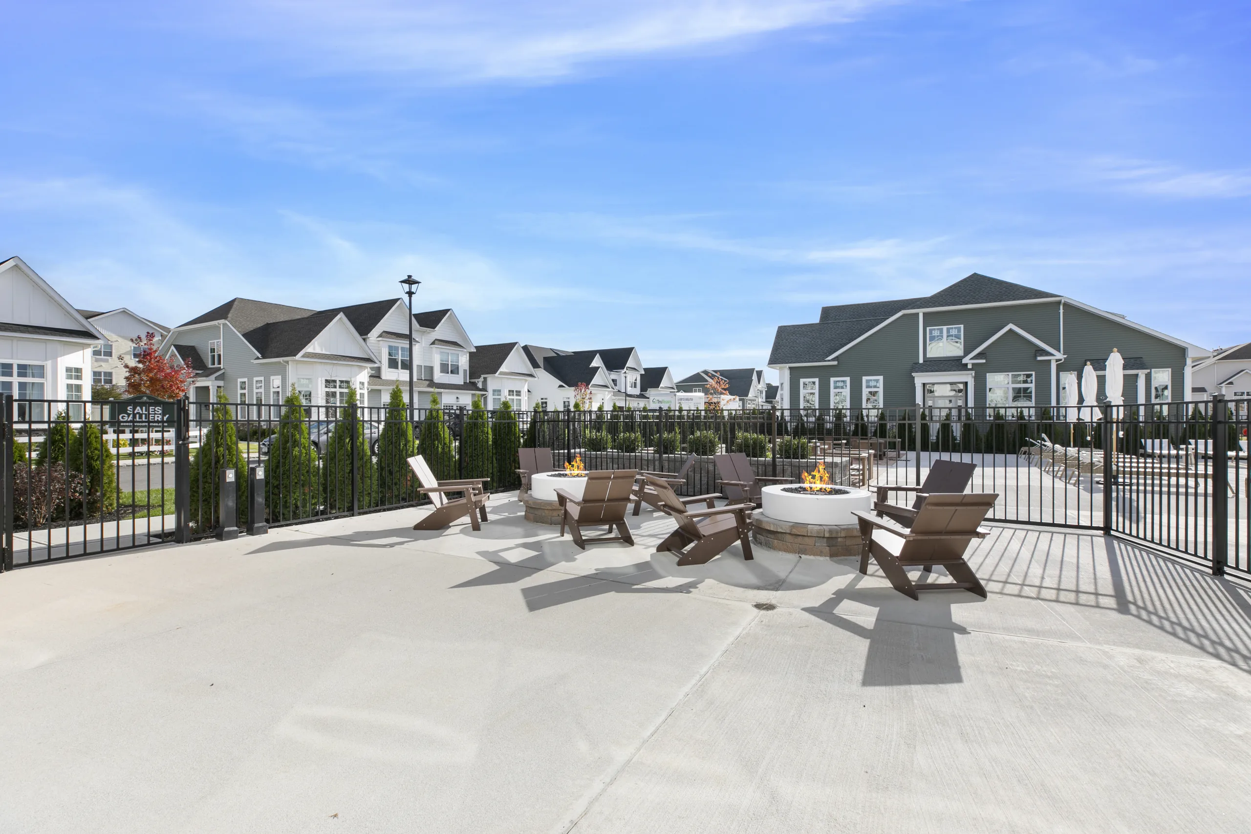 Outdoor patio with two round fire pits surrounded by Adirondack chairs, next to the pool area and the Sales Gallery