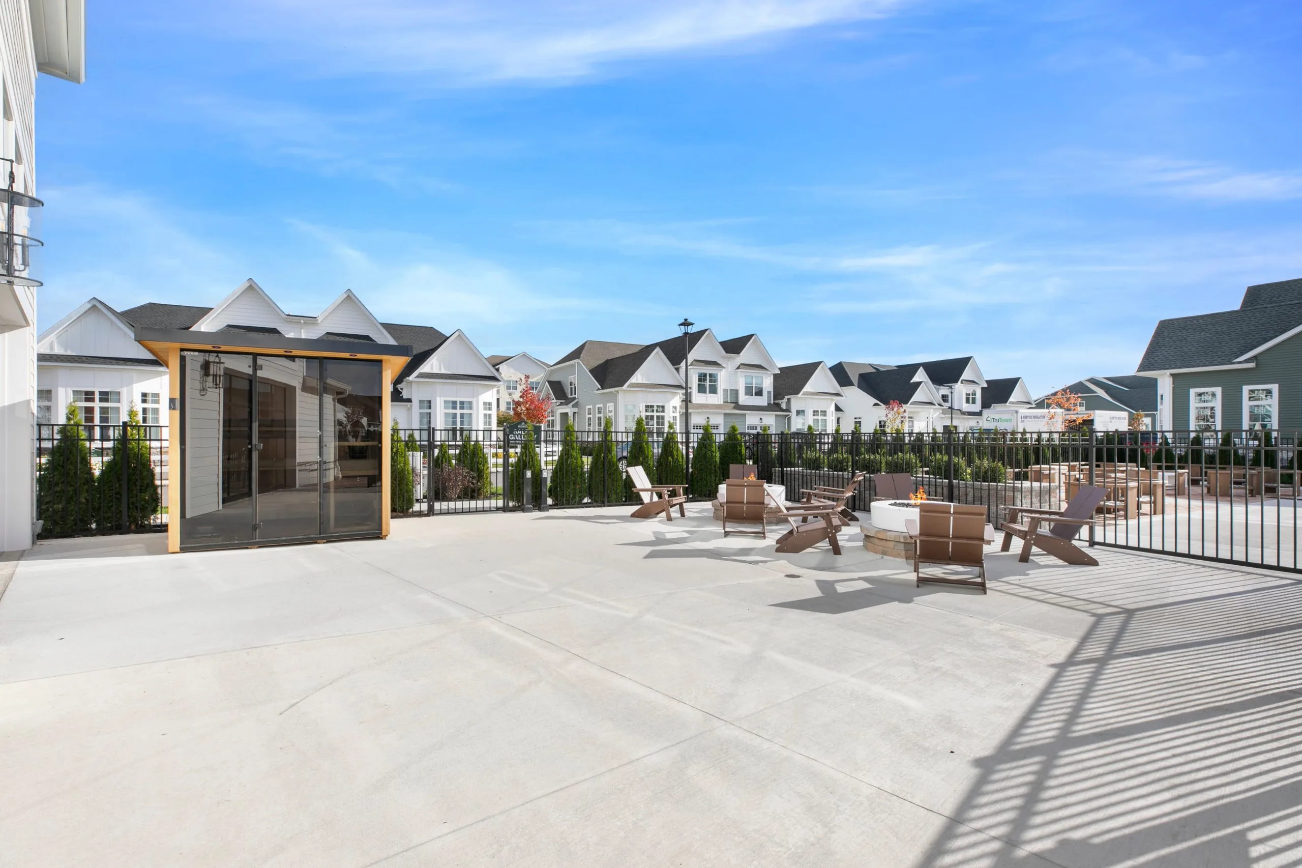 Large clubhouse patio with a glass-front outdoor sauna and fire pit seating, homes in the background
