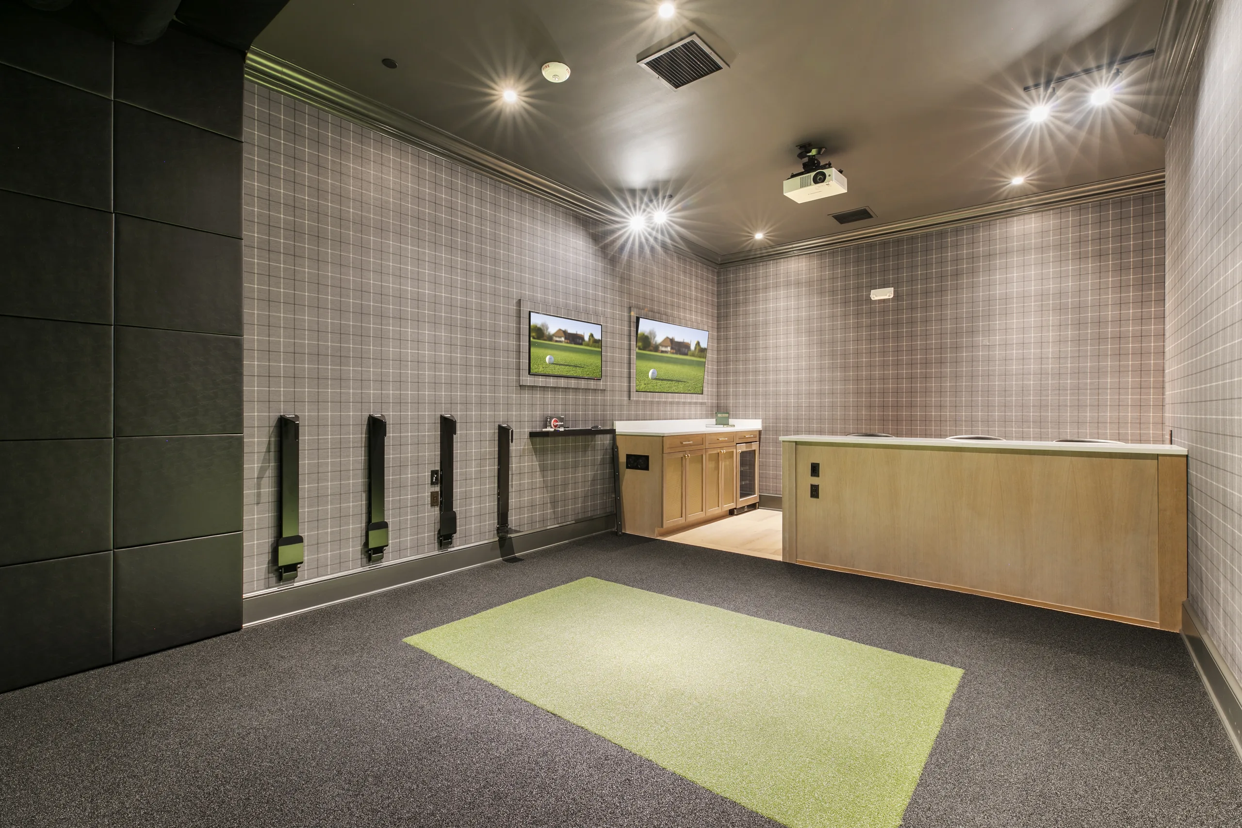 Golf simulator lounge with plaid wallcovering, wall-mounted TVs, club racks, a hitting mat and a wood bar counter