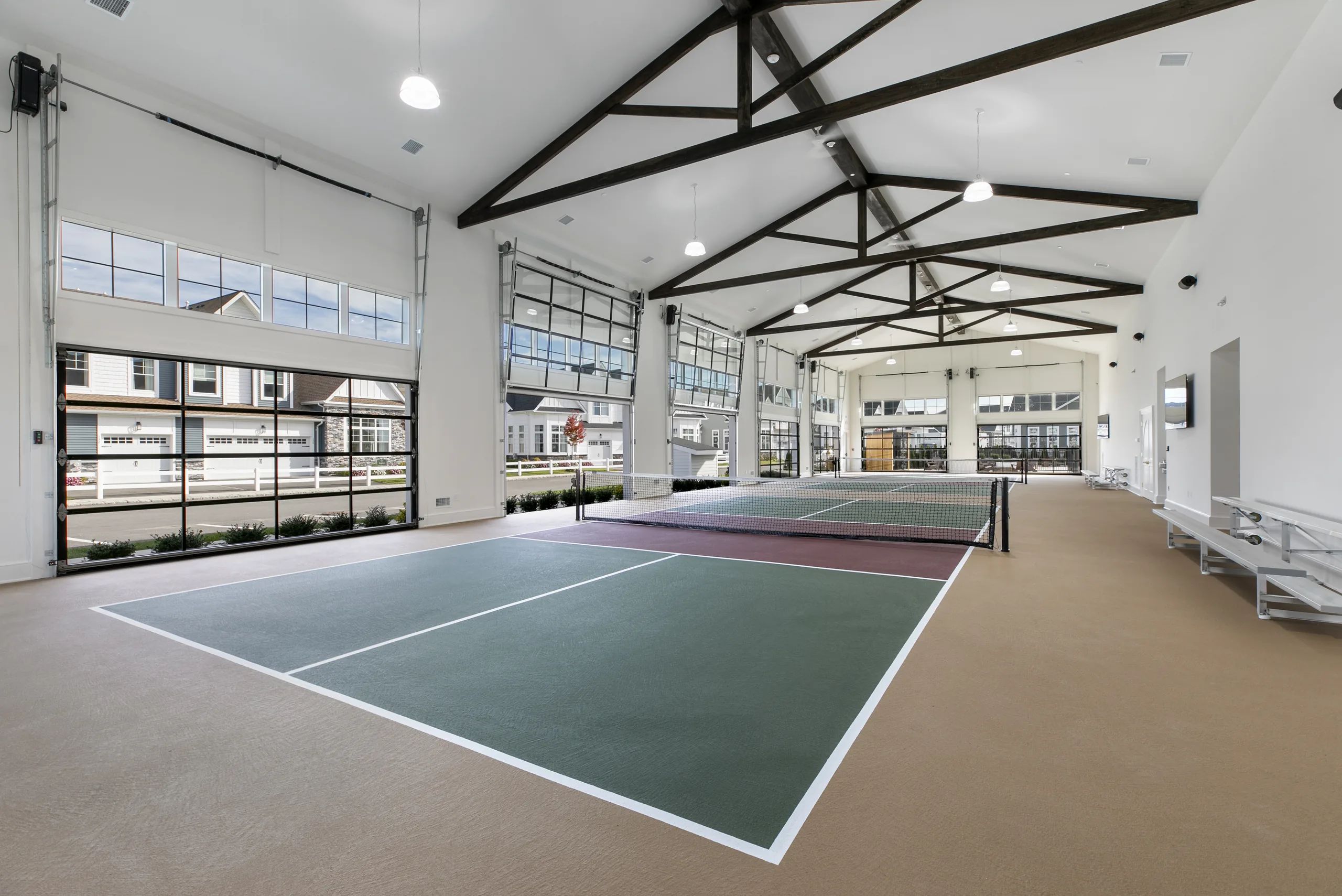 Indoor pickleball pavilion with dark wood trusses, glass garage-style doors and multiple courts