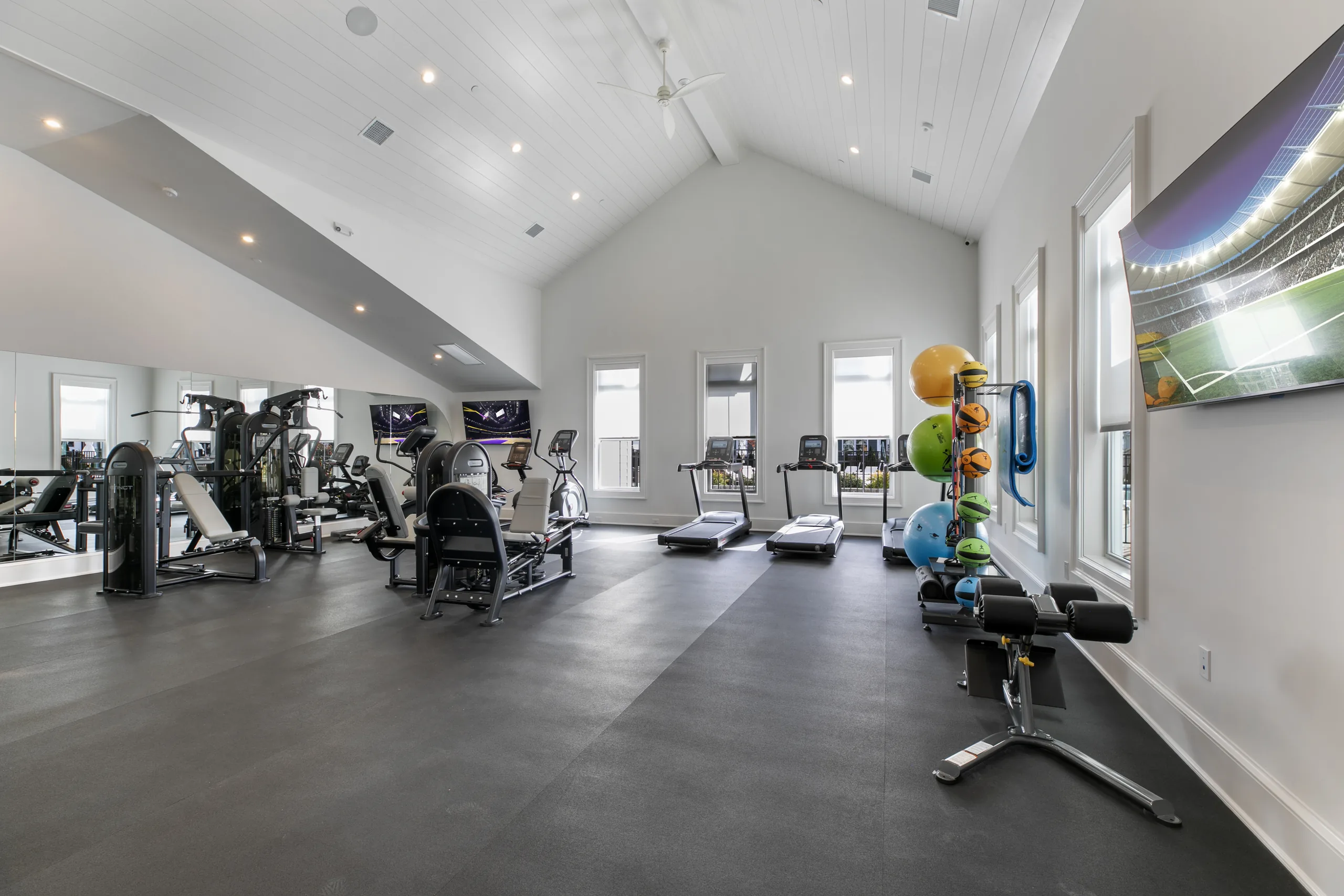 Fitness center with a vaulted shiplap ceiling, treadmills, strength machines, an exercise ball rack and wall-mounted TVs