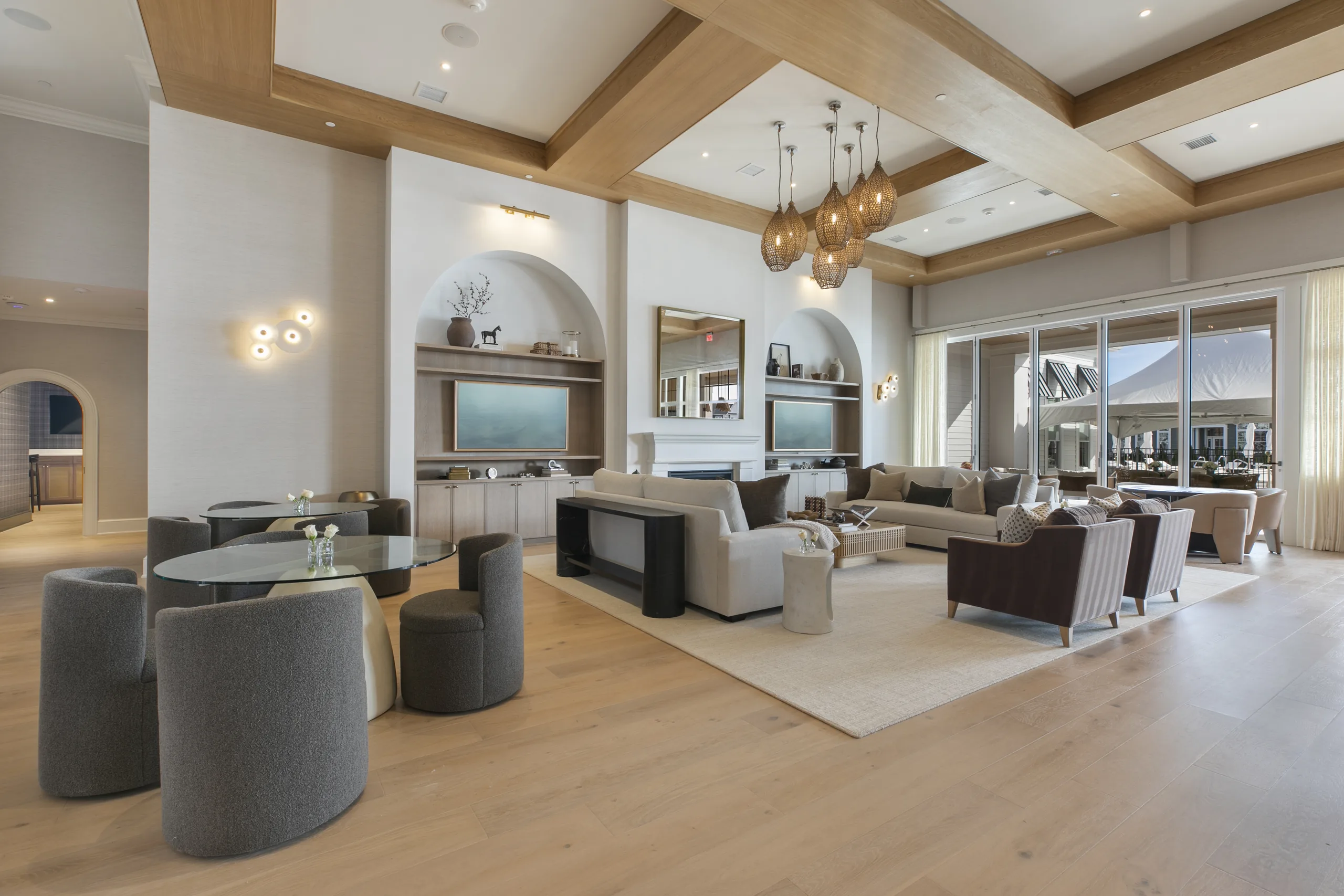 Clubhouse great room with a coffered wood-beam ceiling, woven pendant chandelier, sofas and café tables by folding glass doors