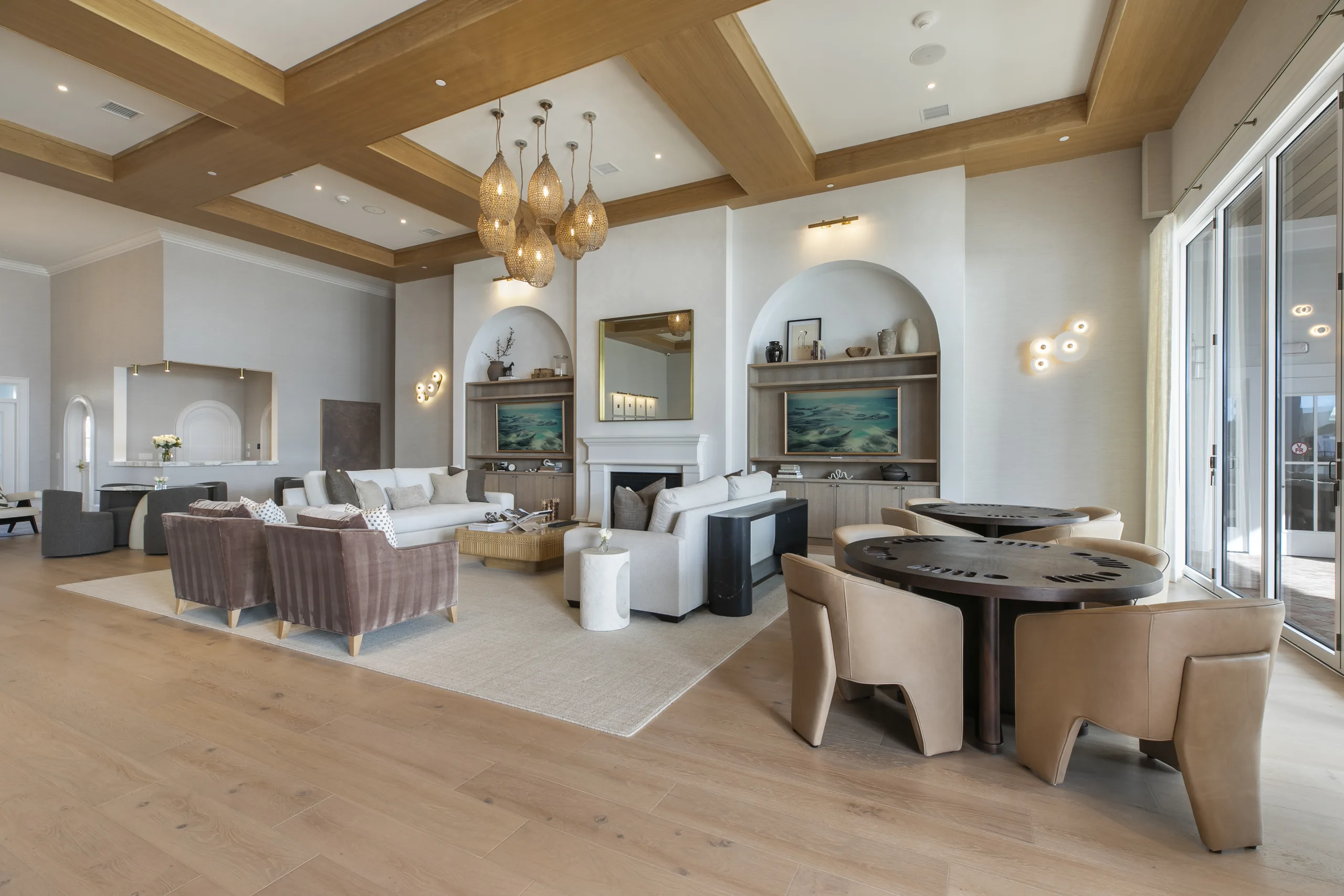 Great room with fireplace seating and round card tables with leather chairs beside floor-to-ceiling glass doors