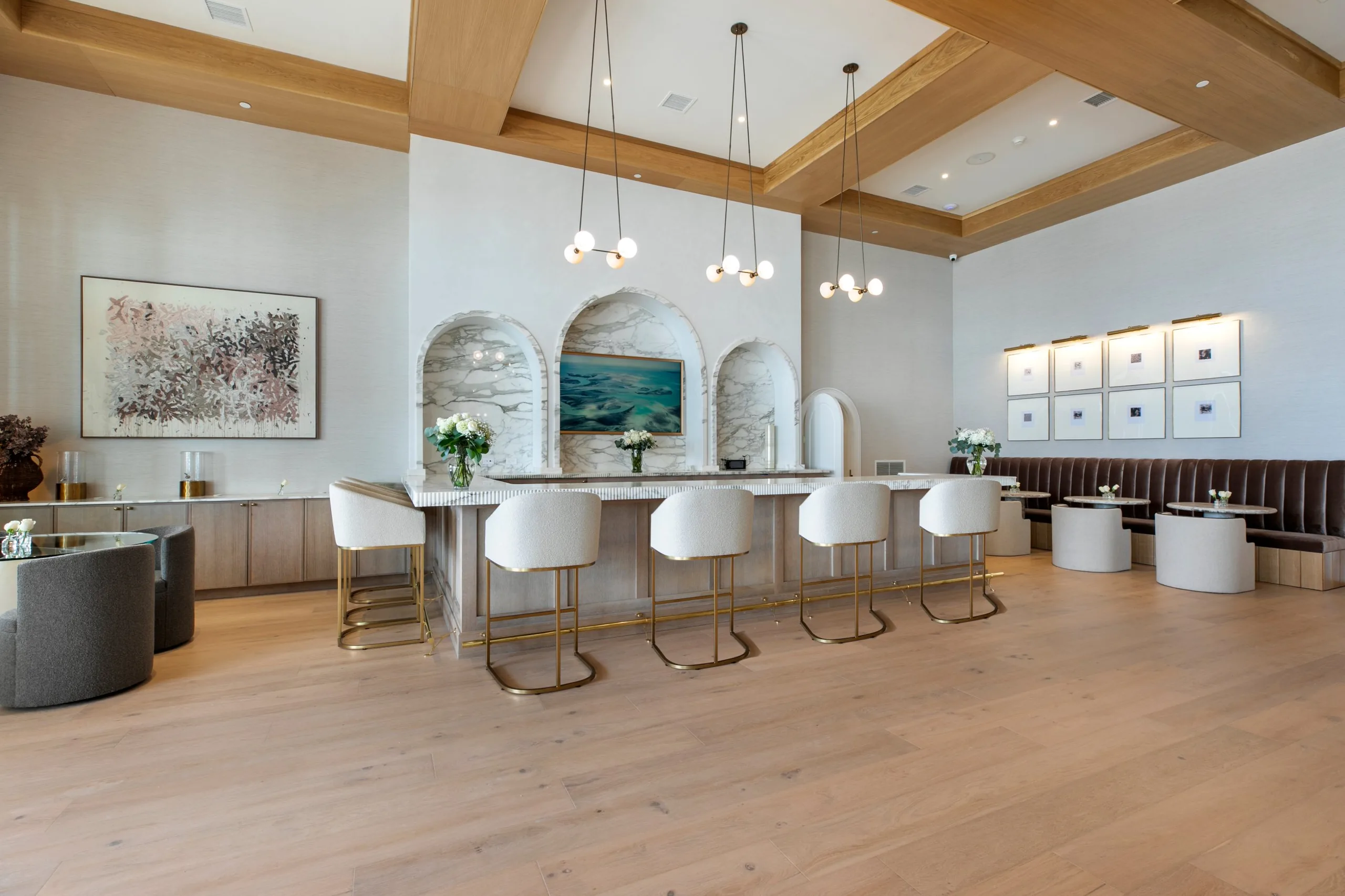 Indoor clubhouse bar with arched marble niches, globe pendant lights, bouclé stools with brass bases and a velvet banquette