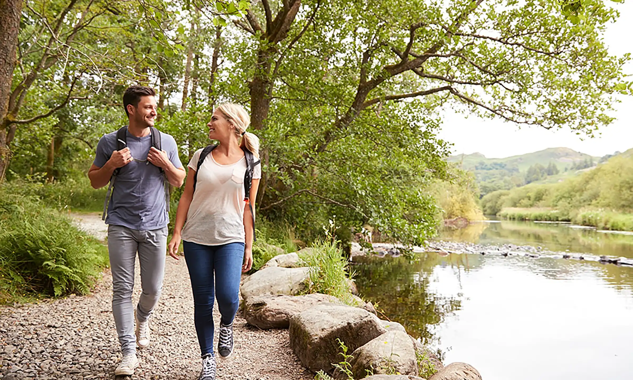 Image of 2 people walking by a lake smiling at each other.