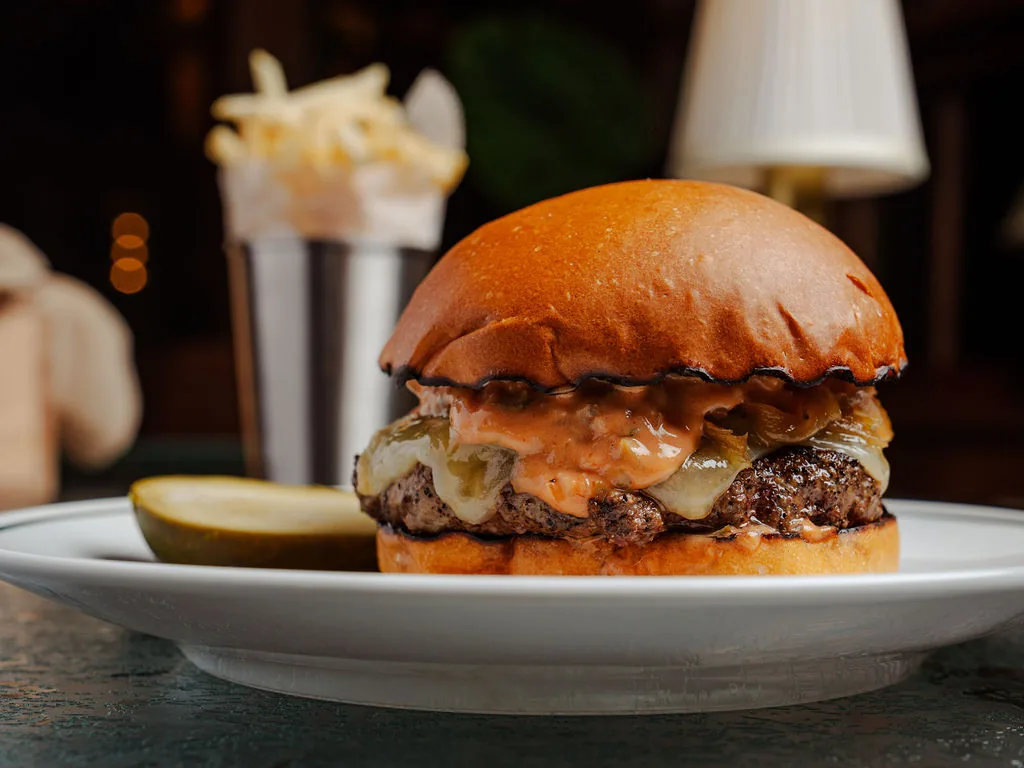 Burger with melted cheese, caramelized onions and special sauce on a toasted brioche bun, served with a pickle and fries at The Comet Club