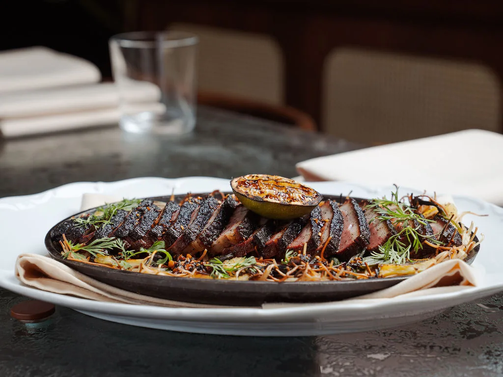 Sliced, char-crusted duck on a cast iron platter at The Comet Club in Westbury