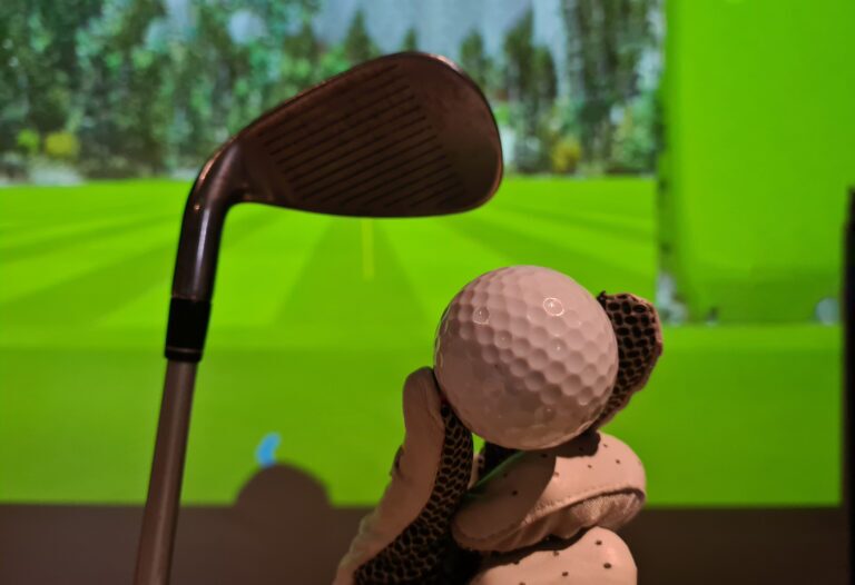 Golfer in glove holds golf ball and club indoors