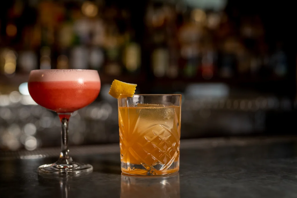 Two cocktails on the bar at Morrissey's Lounge & Bistro, a pink coupe cocktail and an amber old fashioned with lemon twist