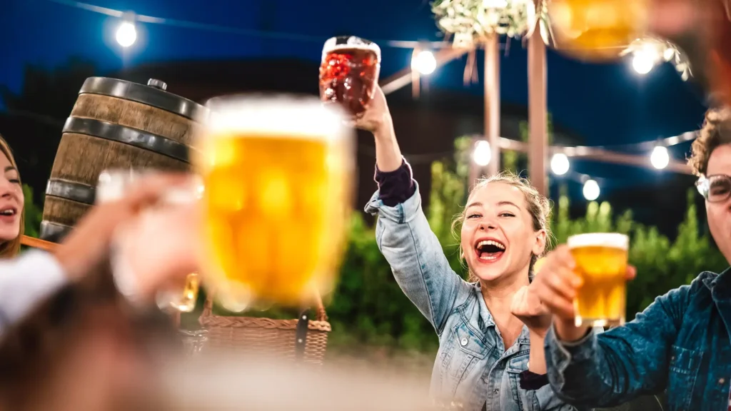 Happy woman clinking and toasting beer at brewery bar restaurant patio with friends at Lake Norman Beerfest.