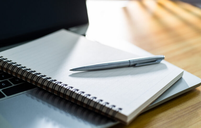 Laptop computer with pen and spiral notebook on desk